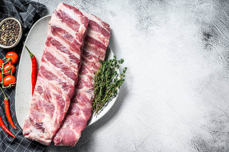 Uncooked Pork spare ribs on a plate garnished with herbs and a chili pepper